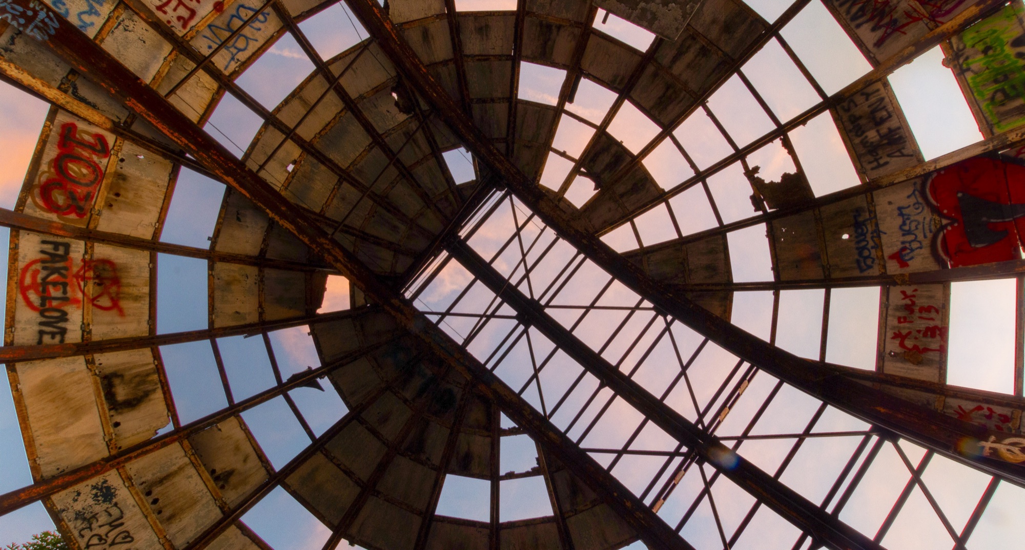 Looking straight up through the ruined glazed dome of an observatory, graffiti on the surviving panels and pink clouds through the empty frames