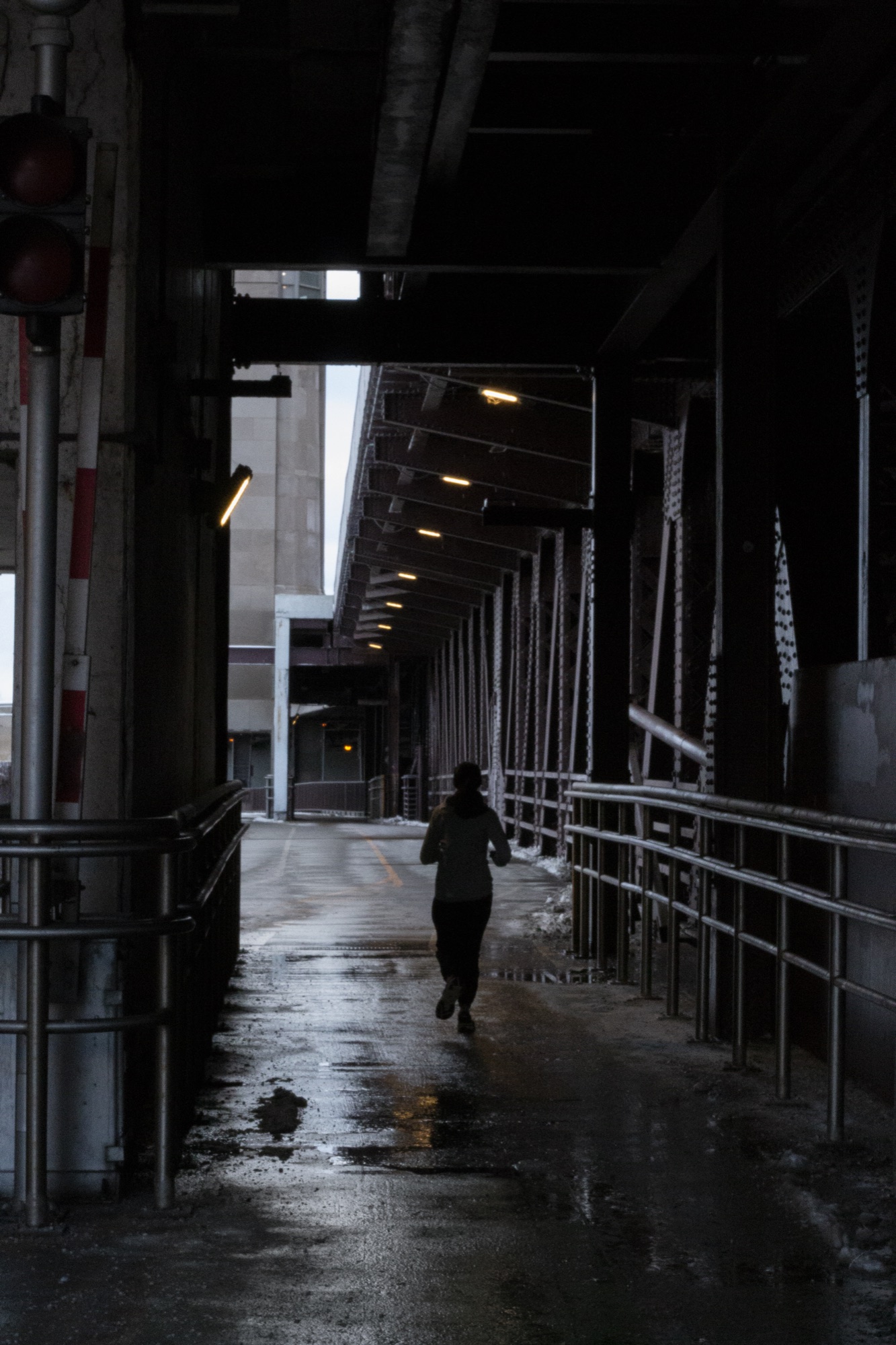 A runner in a dark underpass, strip lights receding above the wet roadway